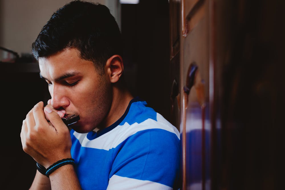 A young man focused on playing the harmonica.