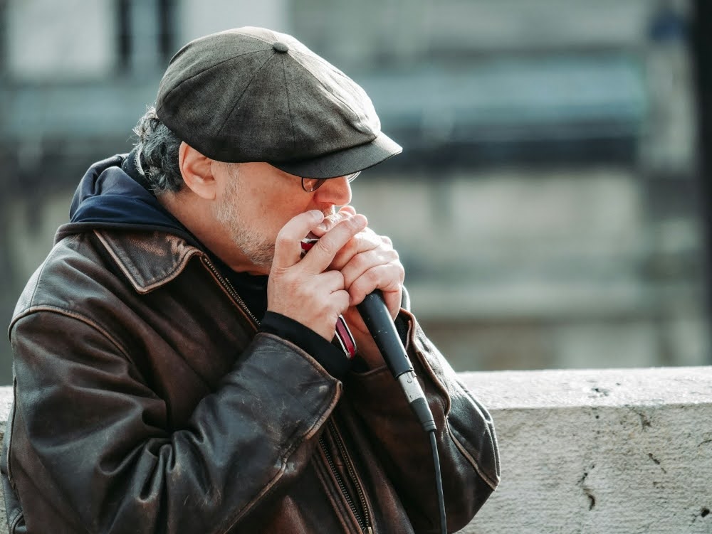 An experienced player holding a mic and playing blues on a harmonica during an outdoor live performance.
