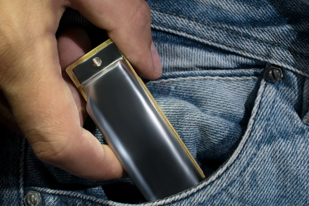 A close-up of a man putting a harmonica in his jeans pocket.